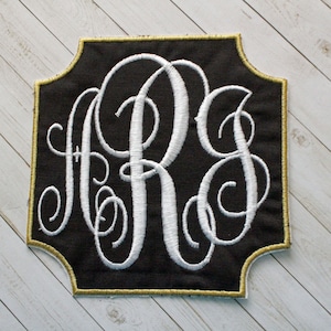 May include: A black fabric monogram with a gold border and white embroidered letters "RJS" in a script font.