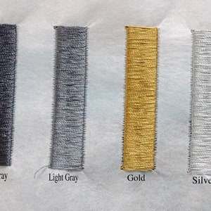 May include: Close-up of four embroidered rectangles in dark gray, light gray, gold, and silver. The rectangles are vertically aligned and labeled with their respective colors. The embroidery is on a white fabric.