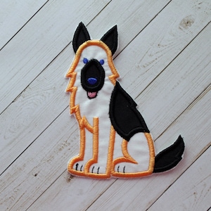 May include: Embroidered patch featuring a cartoon-style German Shepherd dog. The dog has a white body with black patches, orange outline, and black ears. The dog's nose is black, with blue eyes and a pink tongue.