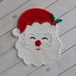 May include: Embroidered Santa Claus face patch with a red hat, white beard, and a smiling expression. The patch features a red nose, black eyes, and a sprig of green holly. The design is outlined in white thread.