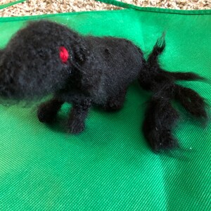 Peut inclure: Un chien en peluche noir et poilu fait main avec des yeux rouges. Le chien est couché sur une surface verte.