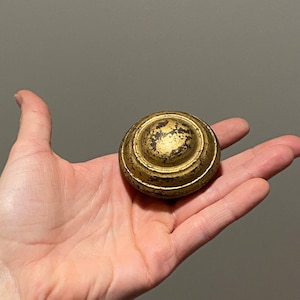 May include: A round, antique-style brass knob with a distressed finish. The knob features concentric circles and a slightly domed top. The aged brass has areas of wear, giving it a vintage appearance. This hardware is suitable for furniture restoration or decorative projects.