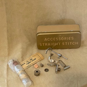 May include: A gold metal tin with the words "ACCESSORIES STRAIGHT STITCH" printed on the lid. The tin contains various sewing machine accessories, including a bobbin, a needle, a small metal tube, and a small piece of thread. There is also a small plastic bottle with a label that reads "HOW TO USE TUBED-OILER".