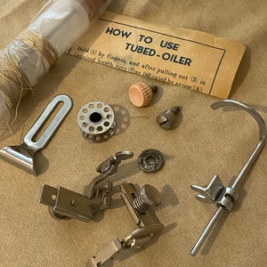 May include: A close-up of a sewing machine accessory kit with instructions on how to use a "TUBED-OILER". The kit includes a metal bobbin, a metal needle, a metal hook, a metal foot, a metal screw, a metal washer, and a plastic tube.