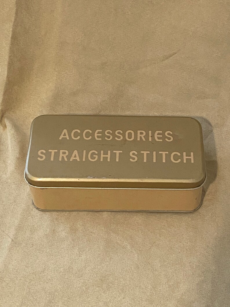 May include: A gold metal tin with the words "Accessories Straight Stitch" printed on the top.