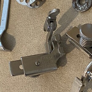 May include: Close-up of a silver sewing machine foot with the text "154 127 SINGER GB BRITAIN" engraved on it.