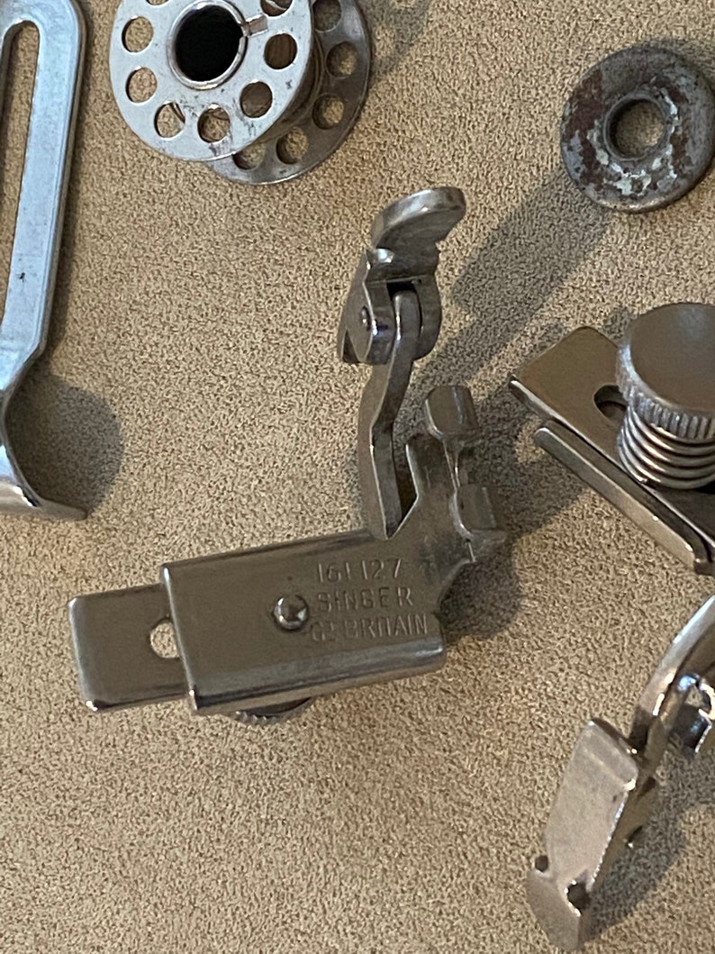 May include: Close-up of a silver sewing machine foot with the text "154 127 SINGER GB BRITAIN" engraved on it.