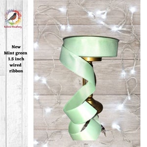 Peut inclure: Un rouleau de ruban vert menthe câblé de 1,5 cm de large. Le ruban est présenté sur un support décoratif sur un fond en bois avec des guirlandes lumineuses blanches.