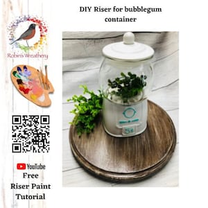 Peut inclure: Un support DIY pour un récipient à chewing-gum. Le support est blanc avec un motif bleu et blanc et un signe 5¢. Le support est sur une base en bois. Un tutoriel de peinture gratuit est disponible sur YouTube.