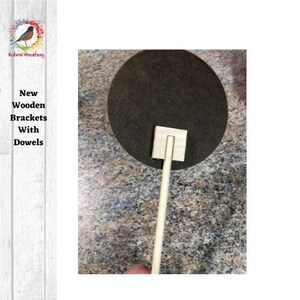 May include: A wooden dowel with a square wooden bracket attached to the top. The dowel is standing upright on a brown surface.