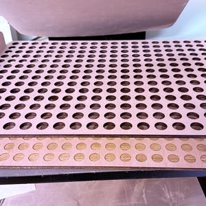 Może przedstawiać: Stos trzech drewnianych tac o jasnobrązowym wykończeniu. Górna taca ma liczne, równomiernie rozmieszczone okrągłe wycięcia. Każda taca ma uchwyt po obu stronach. Tace są ułożone jedna na drugiej.