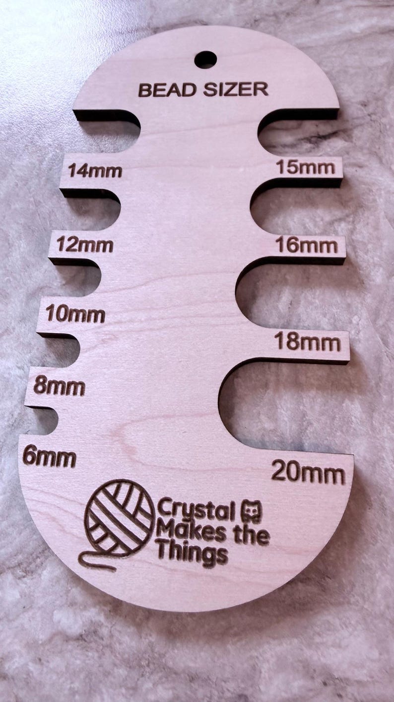 Pu&ograve; includere: Un misuratore di perline in legno con misure da 6 mm a 20 mm. Lo strumento &egrave; etichettato "BEAD SIZER" e include il testo "Crystal Makes the Things". Lo strumento &egrave; progettato per misurare le perline.