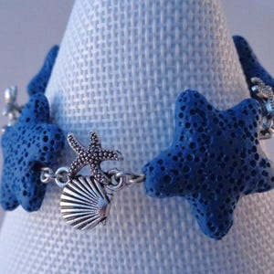 Peut inclure: Un bracelet en pierre de lave bleue avec des breloques en argent en forme d'étoile de mer et de coquillage. Le bracelet est composé de perles de pierre de lave bleue et de breloques en métal argenté.