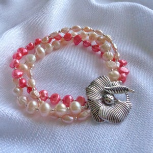 May include: A multi-strand bracelet featuring pink and white pearls with a silver flower charm.