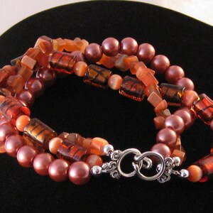 May include: A multi-strand bracelet featuring brown, orange and red beads. The bracelet has a silver clasp.