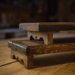May include: Two-tiered wooden display stands with a natural finish. The stands have a dark brown top and light brown supports with a scalloped edge. The wood grain is visible, adding to the rustic aesthetic. Ideal for displaying small items.