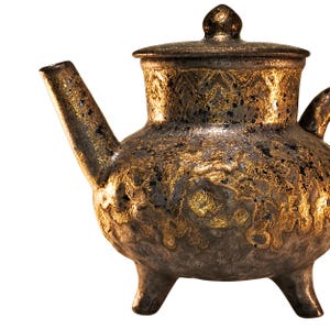 May include: A decorative teapot with a lid, spout, and handle. The teapot is a mix of gold and dark brown, with a textured surface. It has three small feet and a small knob on the lid.