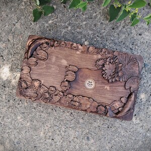 Pu&ograve; includere: Un vassoio rettangolare in legno con intagli intricati di ninfee, fiori di loto e pesci. Il vassoio &egrave; tinto di un colore marrone scuro e presenta un piccolo emblema circolare al centro. Il design &egrave; dettagliato e artistico.