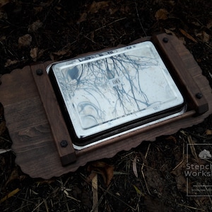 May include: A wooden serving tray with a decorative edge and a stainless steel insert. The tray is dark brown and has a natural wood grain. The insert is shiny and reflects the surrounding environment.