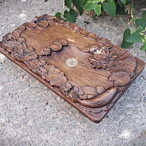 Pu&ograve; includere: Vassoio da t&egrave; rettangolare in legno, tinto di marrone caldo, con intagli intricati di ninfee e pesci. Il vassoio presenta un emblema circolare centrale. Il lavoro a rilievo aggiunge un tocco di eleganza al design.