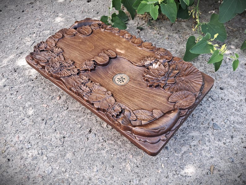 Pu&ograve; includere: Vassoio da t&egrave; rettangolare in legno, tinto di marrone caldo, con intagli intricati di ninfee e pesci. Il vassoio presenta un emblema circolare centrale. Il lavoro a rilievo aggiunge un tocco di eleganza al design.