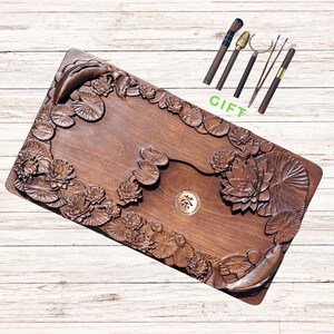 Pu&ograve; includere: Vassoio da t&egrave; rettangolare in legno marrone scuro con fiori di loto, ninfee e carpe koi intagliate. Il set include utensili da t&egrave;. La parola "GIFT" &egrave; scritta in verde.