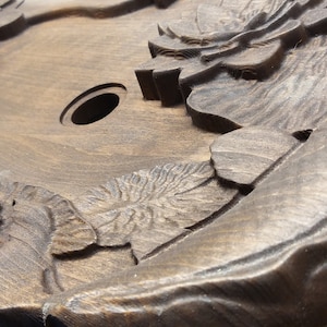 May include: A dark brown wooden tray with intricate carvings of flowers and leaves. The tray has a circular hole in the center.