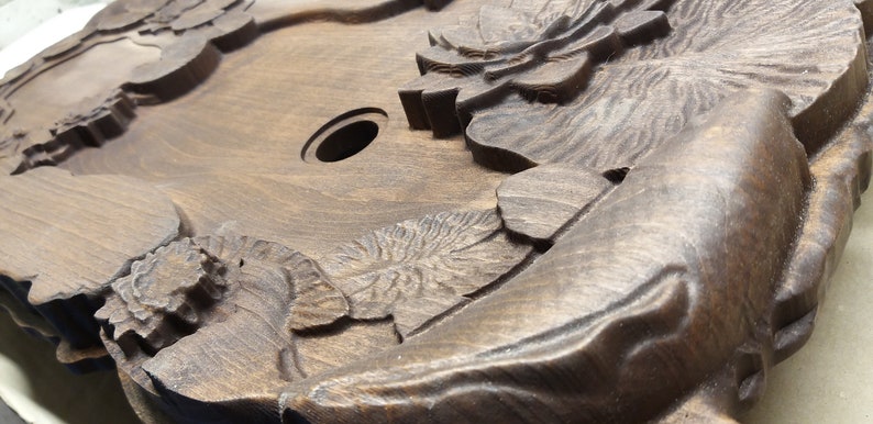 May include: A dark brown wooden tray with intricate carvings of flowers and leaves. The tray has a circular hole in the center.