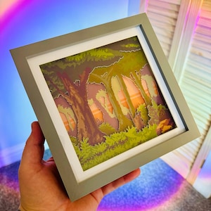 May include: A framed pixel art print of a forest scene with a sunset in the background. The print is in a gray frame with a white mat.