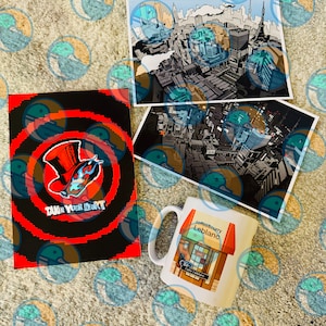 Op de afbeelding: Een verzameling merchandise met artwork uit de videogame Persona 5. Inclusief een mok met een café-ontwerp, twee stadslandschap prints en een notitieboek met de tekst "Take Your Heart" en een masker graphic.