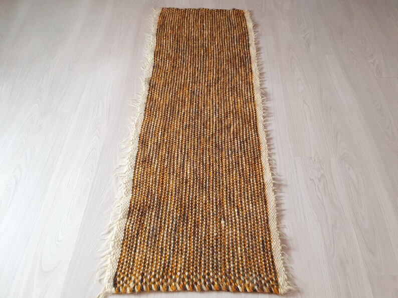 May include: A long, narrow, brown and white woven rug with a fringed edge.