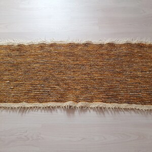 May include: A brown and white woven rug with a fringed edge.