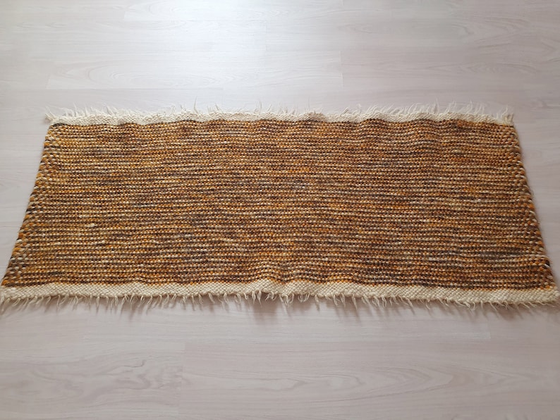 May include: A brown and white woven rug with a fringed edge.