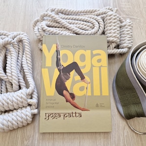 May include: A book titled "Yoga Wall: A manual for Yoga Wall practice" by Dmitry Danilov, with a photo of a person doing yoga on a wall. The book is next to a white cotton rope, a white and green yoga strap, and a white cotton rope with two loops.