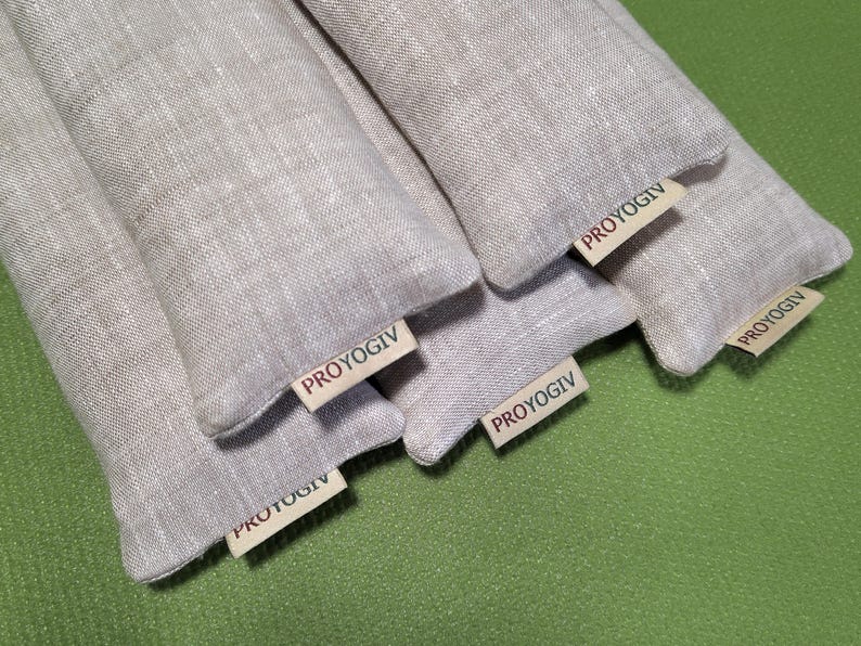 May include: Several light grey linen pouches are displayed, each with a small tag bearing the text "PROYOGIV". The pouches are arranged on a green surface. The tags are visible on the front of each pouch. The pouches appear to be filled.