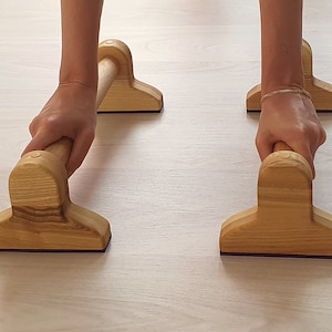 Op de afbeelding: Twee houten push-up bars met een natuurlijke afwerking. De bars zijn ontworpen voor thuis workouts en zijn gemaakt van massief hout.