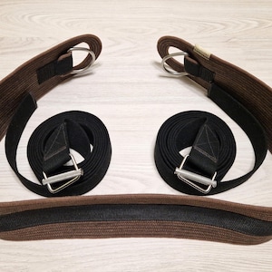 May include: A brown and black equestrian girth with two silver buckles. The girth is made of two layers of webbing, one brown and one black.