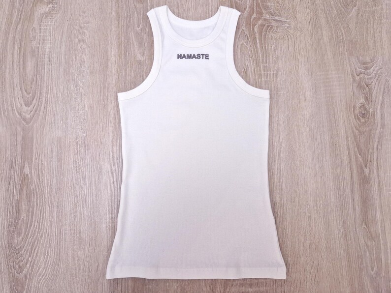 K&ouml;nnte beinhalten: Wei&szlig;es Tanktop mit dem Wort "NAMASTE" auf der Vorderseite.