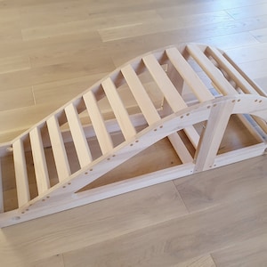 May include: A wooden exercise device with a curved top and a ladder-like structure. The device is made of light-colored wood and has a natural finish.