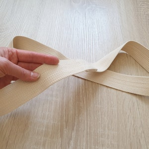 May include: A close-up of a beige cotton webbing strap. The strap is folded in half and held by a hand.