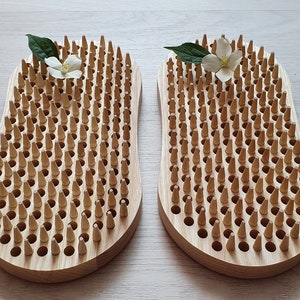 Op de afbeelding: Twee houten voetmassagehulpmiddelen met een raster van kleine houten pinnen. Elk hulpmiddel heeft een bloem bovenop.