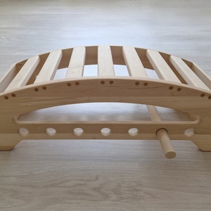 May include: A wooden back support with a curved shape and a series of slats. The support has a wooden handle on the bottom.