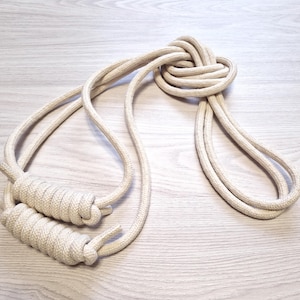 Pode incluir: Uma corda de pular de algodão branco com duas alças amarradas. A corda está amarrada no meio.
