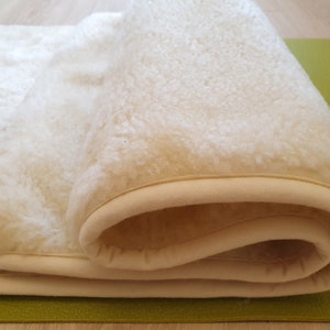 May include: A white sheepskin rug with a cream-colored border. The rug is rolled up and the border is visible.