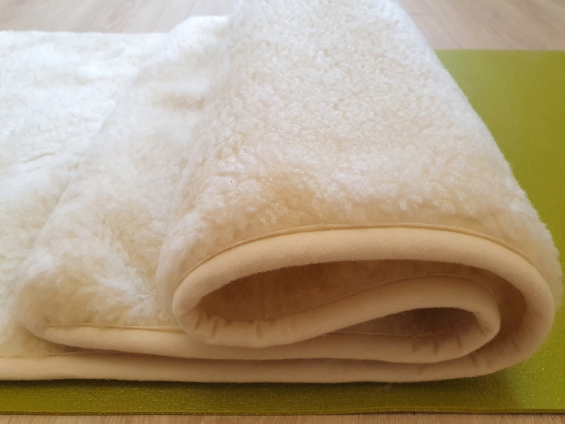 May include: A white sheepskin rug with a cream-colored border. The rug is rolled up and the border is visible.