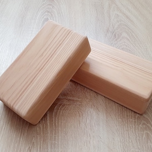 May include: Two wooden blocks, made of light-colored wood, are stacked on top of each other. The blocks are rectangular in shape and have a smooth, polished surface.