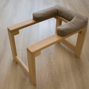 May include: A wooden meditation stool with two padded cushions. The stool is made of natural wood and has a simple, minimalist design.