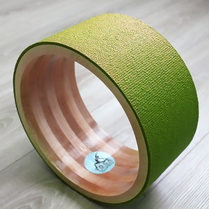 May include: A green foam roller with a wooden core. The roller has a textured surface and is designed for exercise and stretching.