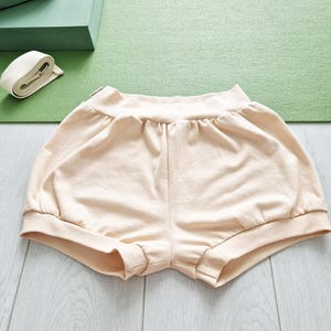May include: A pair of light beige cotton shorts with a gathered elastic waistband and a wide leg.