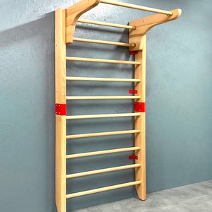 May include: A wooden stall bar with a pull-up bar at the top. The frame is light-colored wood, with horizontal dowels for climbing. Red metal brackets reinforce the frame. The stall bar is mounted on a gray wall.